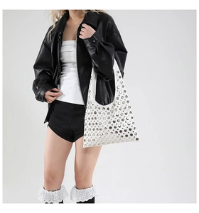 Detail of white leather shoulder bag with silver punk studs on a model in a black jacket
