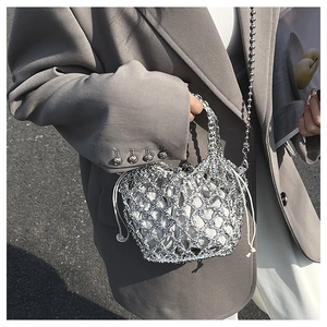Detail der silbernen Web-Eimertasche mit weißem Kordelzugfutter und Perlenkette