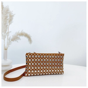 Detail of a brown leather bag with silver studs on a clean surface with dried reeds