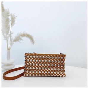 Detail shot of a brown studded crossbody bag with silver rivets on a minimalist white surface