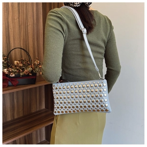 Close-up of light blue shoulder bag with golden rivets worn by model in a stylish setting