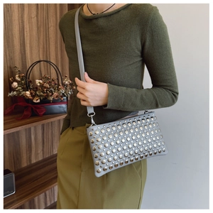 Detail of light blue punk style crossbody bag with silver metal studs worn by model