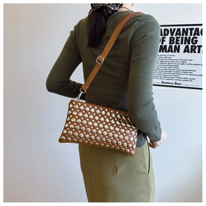 Detailed close-up of brown punk-style handbag featuring silver metal rivets and leather strap