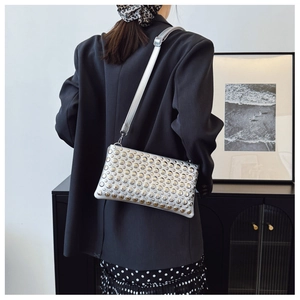 Silver metallic crossbody bag with stud detailing worn by a model in a stylish outfit