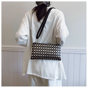 Close-up of black leather shoulder bag with silver punk studs on a female model