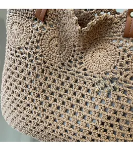 Detail of hand-woven hollow pattern and brown leather handle on a beige tote bag
