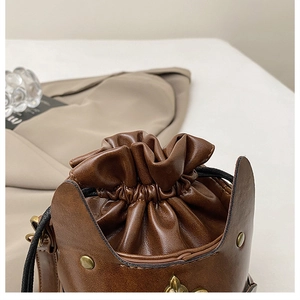 Close-up of vintage brown drawstring bucket bag with brass rivets and metallic shield detail