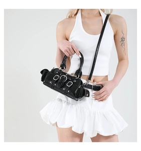 Détail d'un sac de motard en cuir verni noir avec boucles argentées porté par un mannequin