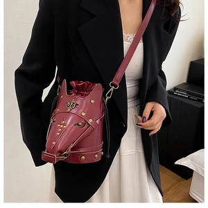 Detail of burgundy leather horse-head bucket bag with gold rivets worn by a model