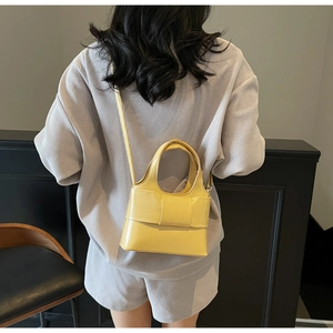 Détail d'un sac seau jaune vif avec nœud papillon porté par un mannequin en décor moderne