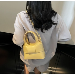 Détail d'un sac seau jaune avec grand nœud, porté en bandoulière sur un sweat gris