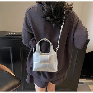 Sac à main argenté métallique avec bandoulière porté par un mannequin sur fond sombre