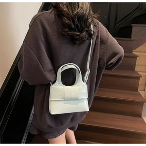 Détails d'un sac seau vert clair avec nœud porté en bandoulière sur un vêtement sombre