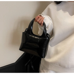 Détail du sac seau en cuir verni noir avec un grand nœud décoratif et une bandoulière