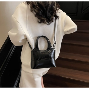 Modèle portant un sac à main noir verni avec nœud à l'épaule sur un escalier en bois