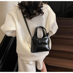 Détail du sac bandoulière en cuir noir brillant avec un grand nœud sur un mannequin