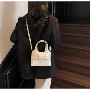 Détail d'un sac seau blanc crème avec un nœud décoratif porté par un mannequin
