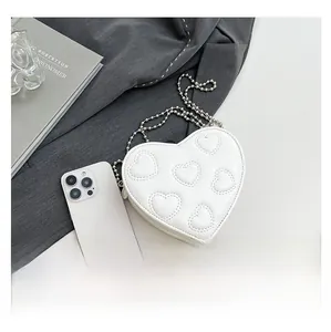Close-up of white heart-shaped mini bag with chain and smartphone for size scale