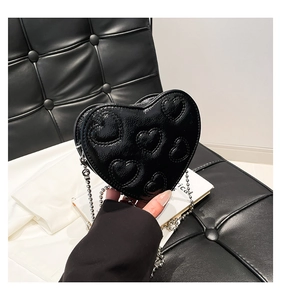 Close-up of black patent heart-shaped crossbody bag with embossed heart textures and silver chain