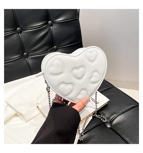 Detail of white heart-shaped crossbody bag featuring quilted patterns and silver bead chain
