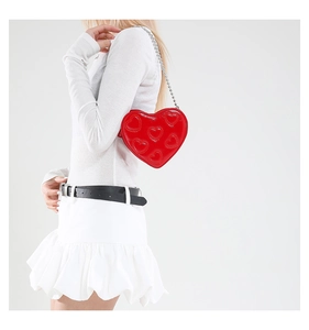 Detail of red heart-shaped crossbody bag with quilted texture and silver chain strap