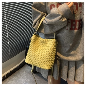 Close-up of yellow woven leather bucket bag with slim shoulder strap and woven texture