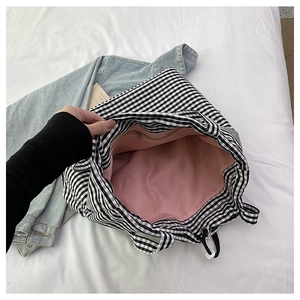 Detail of checkered tote bag with pink lining, interior zipper pocket, and drawstring closure
