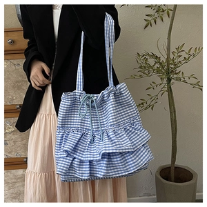 Close-up of blue plaid canvas tote bag featuring layered ruffles and drawstring closure