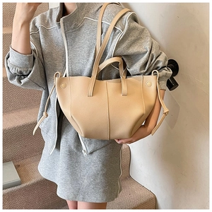 Detail view of beige lychee texture tote bag with stylish side drawstring on gray outfit
