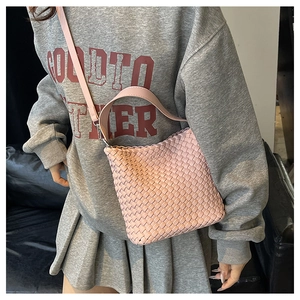 Detail view of a pink woven bucket bag with matching leather strap on a shoulder