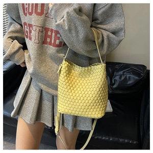 Detailed view of yellow woven bucket bag with leather strap on a model outfit