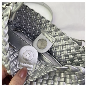 Detail view of woven silver handbag showing magnetic closure and internal zipper pocket