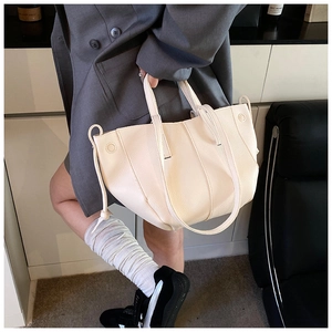 Detailansicht der cremefarbenen Ledertasche mit dekorativen Kordelzügen auf grauem Anzug