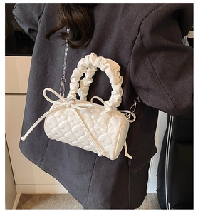 Close-up of white heart-quilted cylinder bag with ribbon bow and metal chain strap