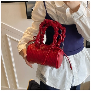 Close-up of heart-quilted red cylinder bag with ruched handle and bow tassels detail