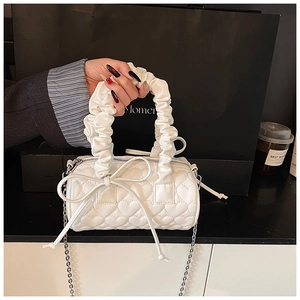 Detail of white heart-quilted barrel bag featuring scrunchie handle and silver chain