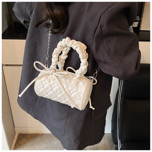 Detail of white cylinder bag featuring heart quilting and ruched handle on model