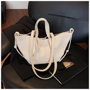 Detail einer cremefarbenen Ledertasche mit breiten Henkeln und Gurt auf einem Blazer