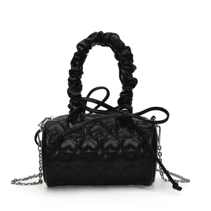Detail of black cylinder bag featuring quilted heart patterns and a ruffled top handle
