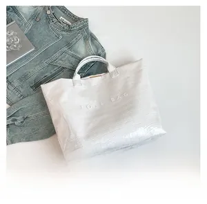 Detailed view of white crocodile texture surface with embossed TOTE BAG lettering on bag