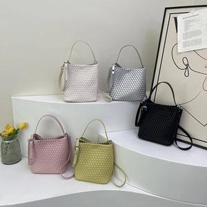Woven leather bucket bags in multiple colors displayed on elegant white steps with tulips