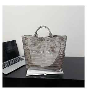 Close-up of grey crocodile embossed texture and white TOTE BAG text on fashionable tote