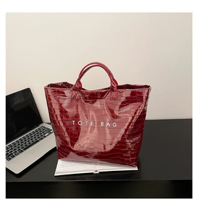 Macro detail of wine red tote bag featuring glossy crocodile texture and bold white lettering