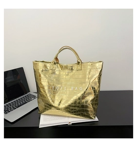Detail view of the metallic gold crocodile texture and TOTE BAG lettering on a laptop desk