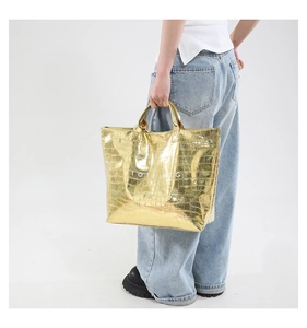 Close-up of golden crocodile embossed tote bag with TOTE BAG text shown on a model