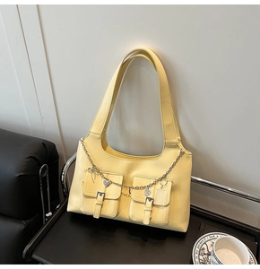 Detail of yellow shoulder bag featuring silver buckle pockets and decorative metal chain