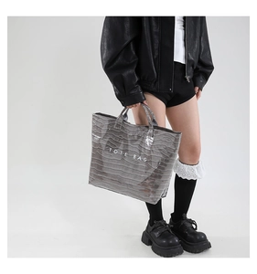 Gray crocodile-patterned tote bag with white TOTE BAG lettering held by model