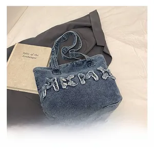 Close-up of blue denim tote bag featuring large frayed letter patchwork and sturdy handles