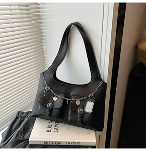 Detail of black tote bag featuring double pockets with silver buckles and heart chain strap