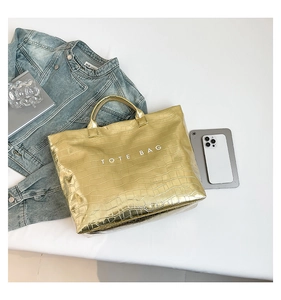 Detailed close-up of metallic gold tote bag featuring crocodile pattern and TOTE BAG text